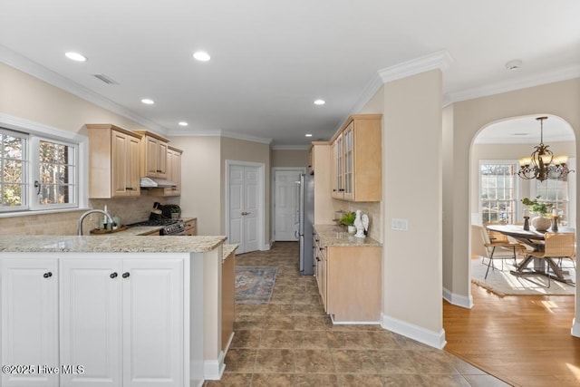 kitchen with light brown cabinetry, light stone counters, ornamental molding, kitchen peninsula, and decorative backsplash