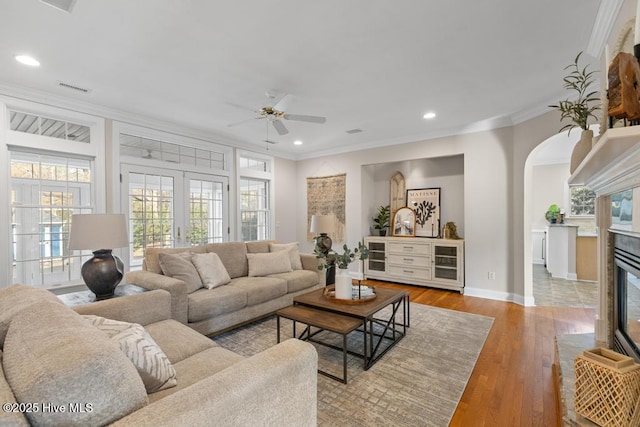 living area with crown molding, a ceiling fan, a wealth of natural light, visible vents, and arched walkways