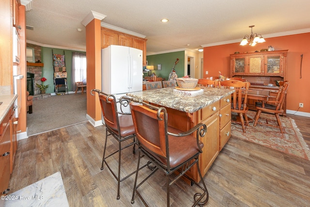 kitchen with crown molding, hardwood / wood-style floors, a center island, light stone counters, and a fireplace