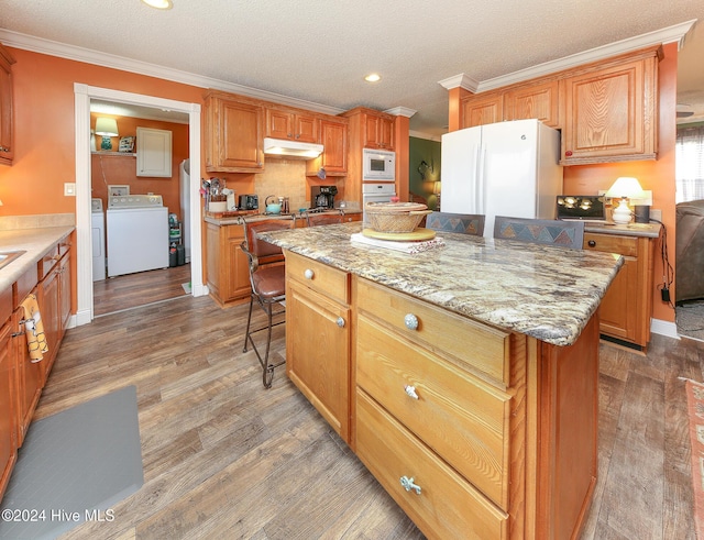 kitchen with a kitchen island, hardwood / wood-style floors, ornamental molding, washer and clothes dryer, and white appliances