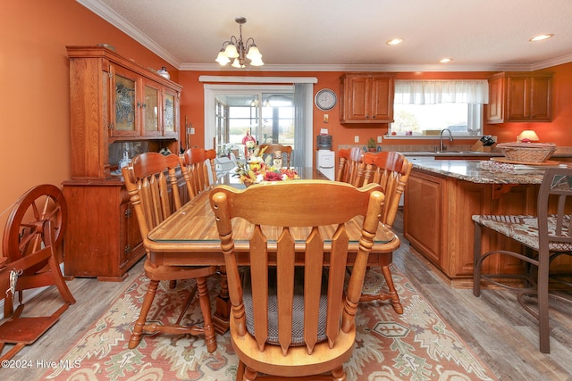 dining space with crown molding, sink, a chandelier, and light hardwood / wood-style flooring