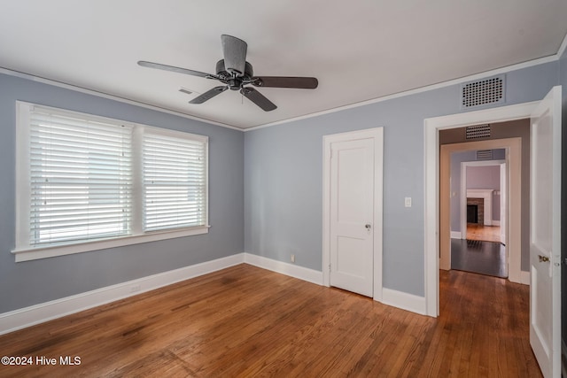 unfurnished bedroom featuring a fireplace, ceiling fan, crown molding, and dark hardwood / wood-style flooring