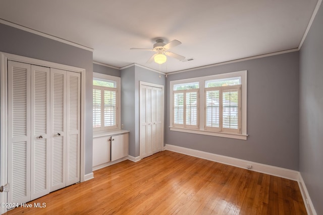 unfurnished bedroom with ceiling fan, multiple windows, two closets, and light hardwood / wood-style floors