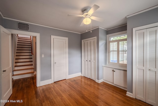 unfurnished bedroom with hardwood / wood-style flooring, two closets, ceiling fan, and crown molding