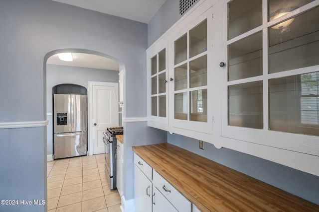 kitchen featuring white cabinetry, stainless steel appliances, light tile patterned floors, and butcher block countertops