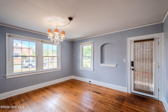 unfurnished dining area featuring wood-type flooring, a notable chandelier, a healthy amount of sunlight, and crown molding