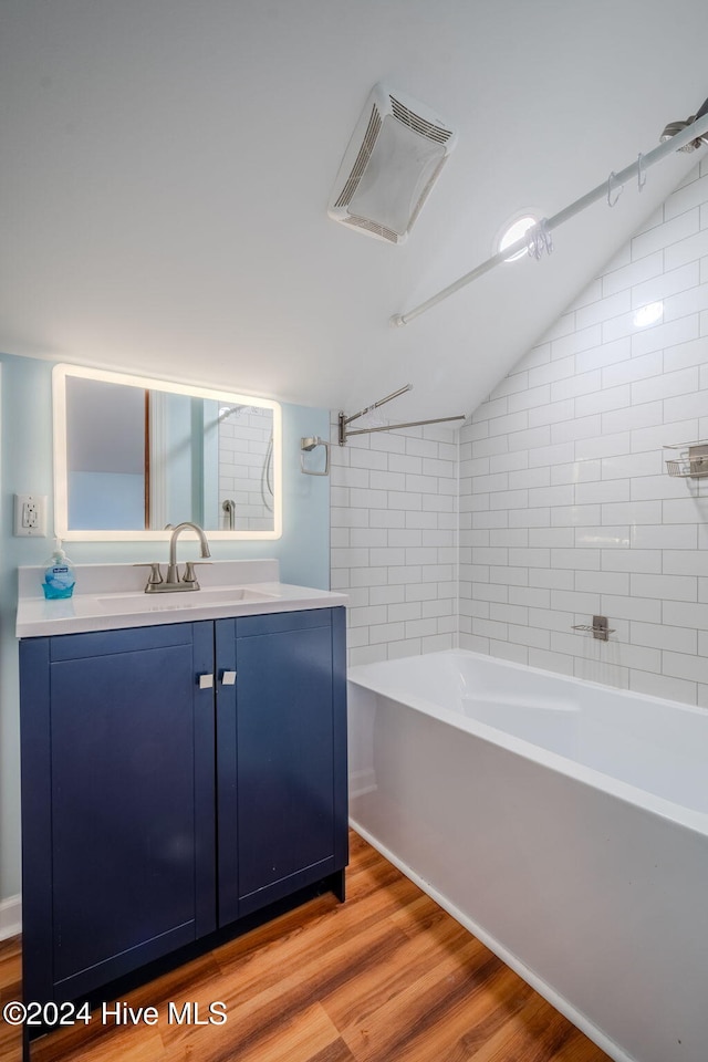 bathroom with vanity, wood-type flooring, tiled shower / bath, and lofted ceiling