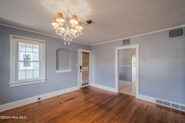 empty room with ornamental molding, a notable chandelier, and hardwood / wood-style flooring