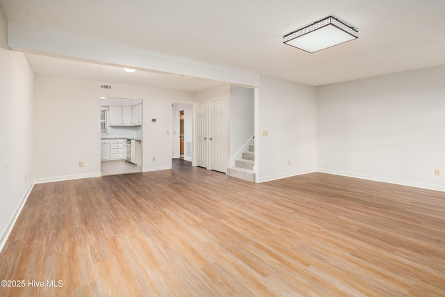 spare room with light wood-type flooring, baseboards, and stairs