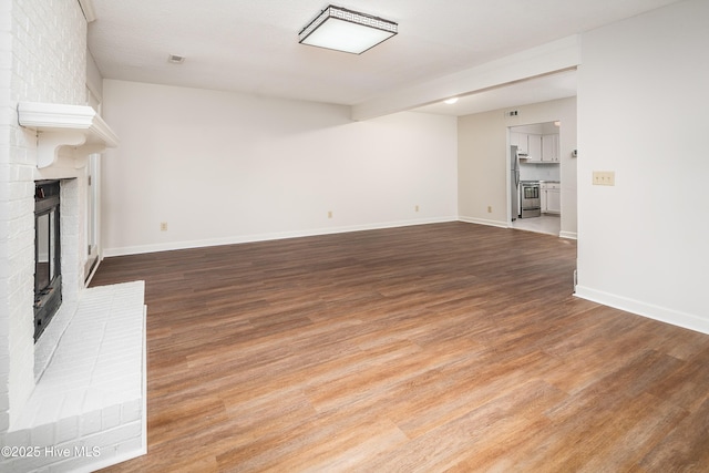 unfurnished living room with a brick fireplace, baseboards, and wood finished floors