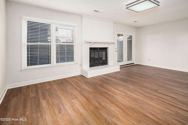 unfurnished living room with a fireplace, wood finished floors, visible vents, and baseboards