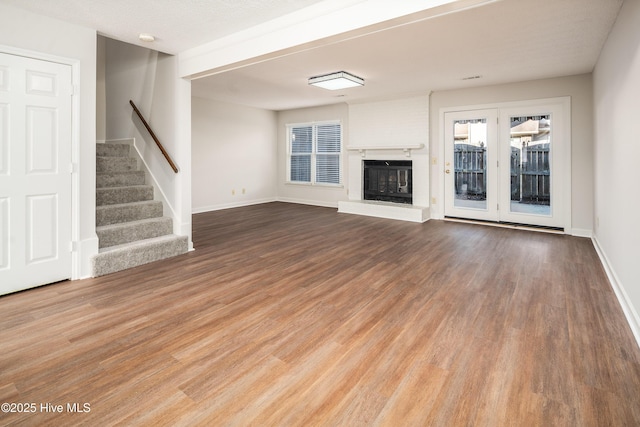 unfurnished living room with light wood-style flooring, stairs, baseboards, and a glass covered fireplace