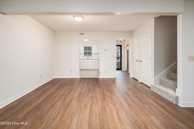 empty room featuring baseboards, stairway, and light wood-style floors