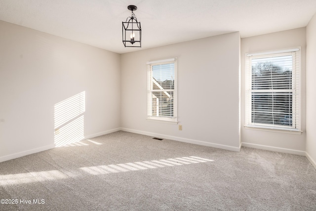 carpeted spare room with a notable chandelier and baseboards