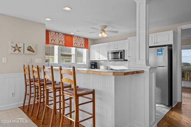 kitchen featuring kitchen peninsula, decorative columns, a breakfast bar, white cabinetry, and appliances with stainless steel finishes