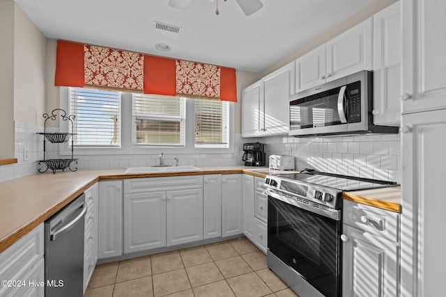 kitchen featuring tasteful backsplash, stainless steel appliances, light tile patterned floors, sink, and white cabinets