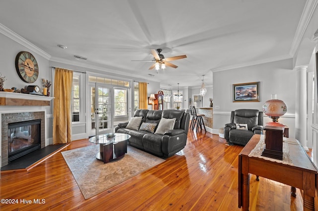 living room with ornamental molding, ornate columns, light hardwood / wood-style floors, a brick fireplace, and ceiling fan