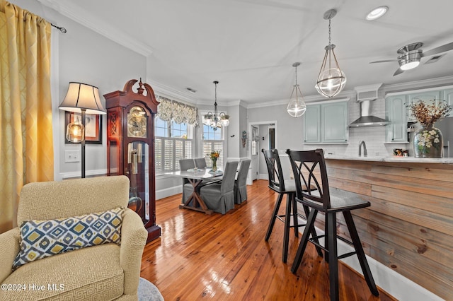 dining area with ornamental molding, ceiling fan with notable chandelier, wood-type flooring, and sink