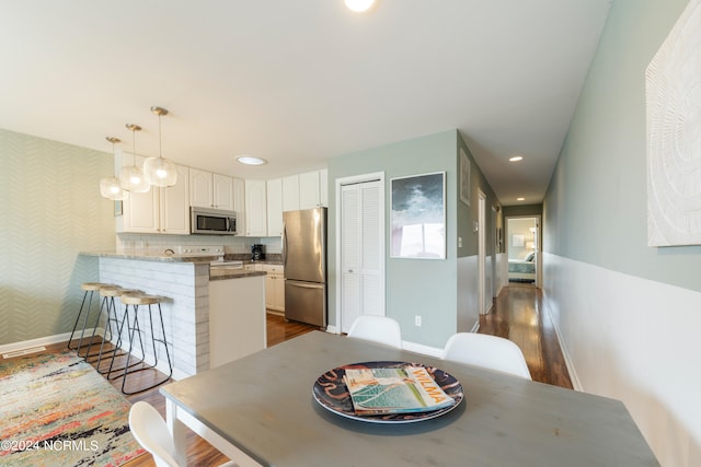 kitchen featuring white cabinetry, appliances with stainless steel finishes, decorative light fixtures, dark hardwood / wood-style flooring, and kitchen peninsula