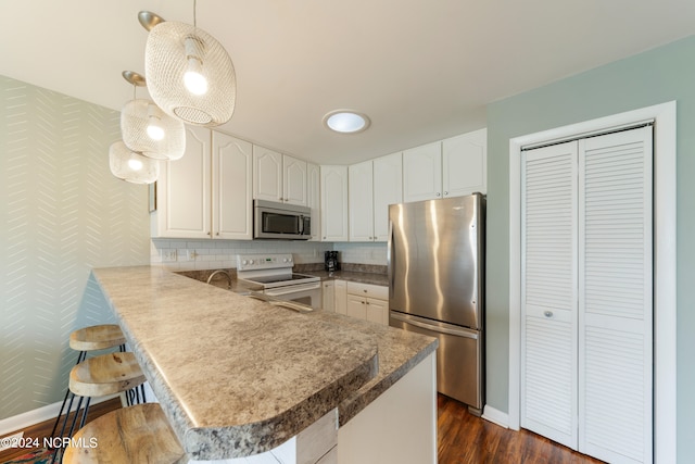 kitchen with stainless steel appliances, white cabinetry, hanging light fixtures, a breakfast bar, and kitchen peninsula