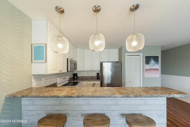 kitchen featuring white cabinets, kitchen peninsula, tasteful backsplash, appliances with stainless steel finishes, and decorative light fixtures