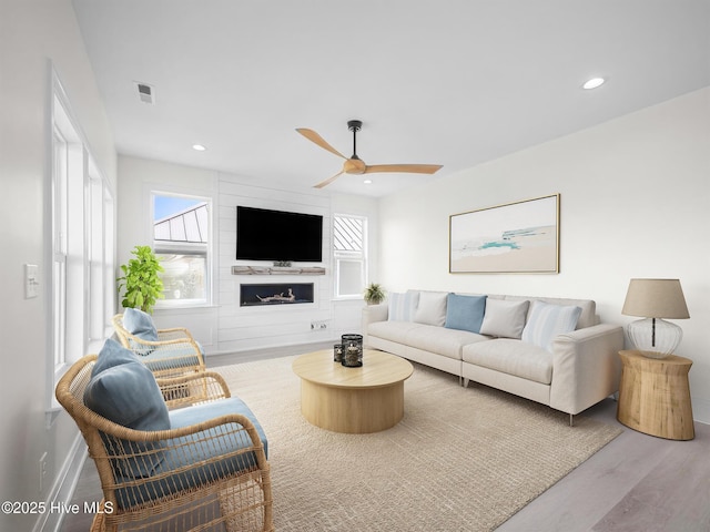 living area featuring a ceiling fan, visible vents, plenty of natural light, and wood finished floors