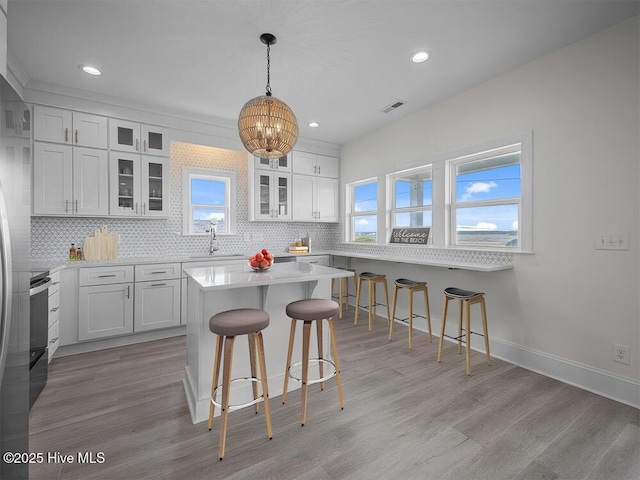 kitchen with glass insert cabinets, visible vents, white cabinets, a center island, and decorative light fixtures