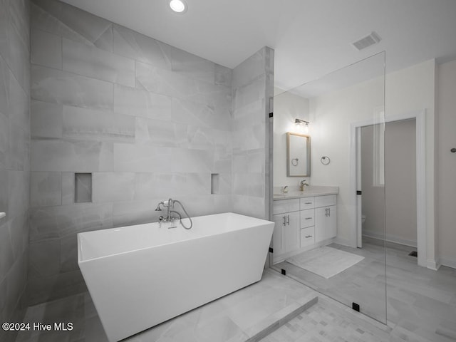 bathroom featuring toilet, vanity, visible vents, tile walls, and a soaking tub