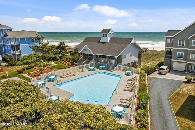 view of pool featuring a water view, a view of the beach, and a patio