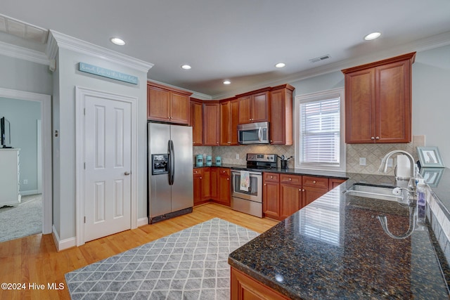 kitchen with stainless steel appliances, sink, ornamental molding, dark stone counters, and light wood-type flooring