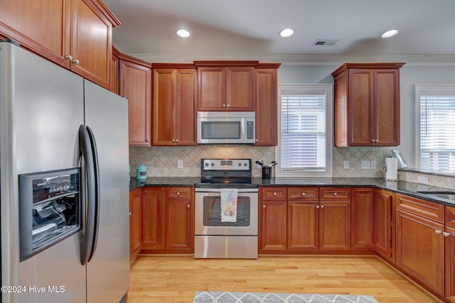 kitchen with appliances with stainless steel finishes, light hardwood / wood-style floors, crown molding, and backsplash