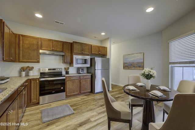 kitchen with light hardwood / wood-style floors, light stone countertops, appliances with stainless steel finishes, and tasteful backsplash