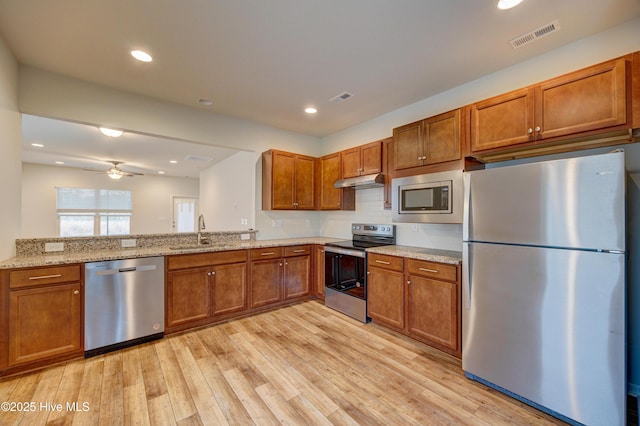 kitchen with sink, ceiling fan, light stone countertops, light wood-type flooring, and stainless steel appliances