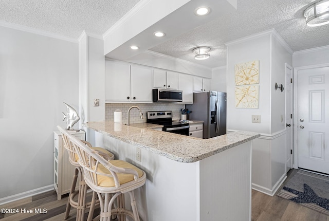 kitchen with white cabinetry, kitchen peninsula, appliances with stainless steel finishes, and a breakfast bar