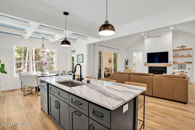 kitchen with light stone countertops, pendant lighting, a center island with sink, and light hardwood / wood-style floors