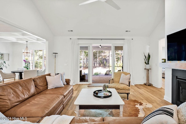 living room with ceiling fan with notable chandelier, light hardwood / wood-style floors, and high vaulted ceiling