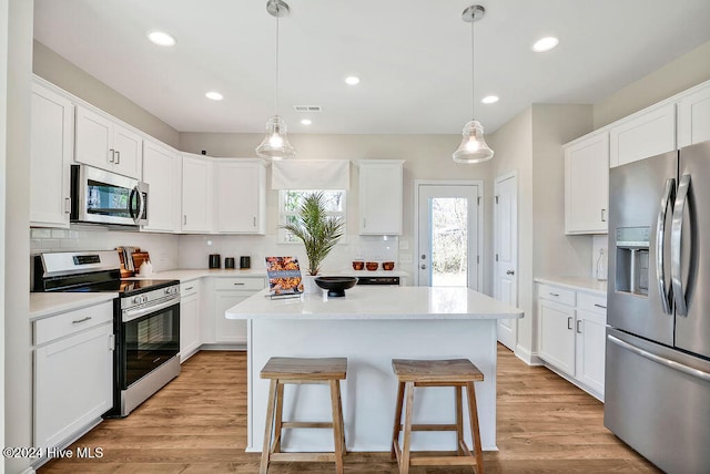 kitchen with white cabinets, appliances with stainless steel finishes, a kitchen island, and light hardwood / wood-style flooring