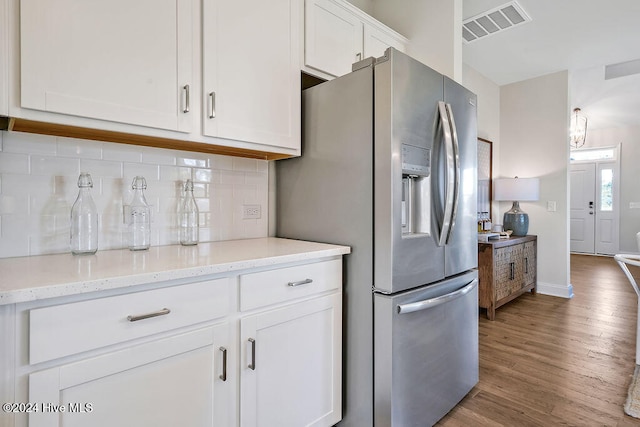 kitchen featuring hardwood / wood-style flooring, white cabinetry, light stone countertops, stainless steel fridge with ice dispenser, and decorative backsplash