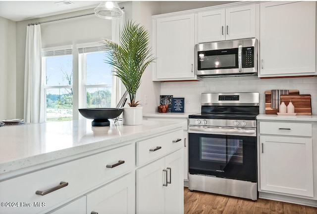 kitchen with tasteful backsplash, light stone counters, stainless steel appliances, white cabinetry, and light hardwood / wood-style flooring