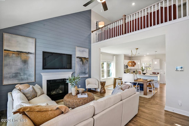 living room with high vaulted ceiling, light hardwood / wood-style floors, wood walls, and ceiling fan