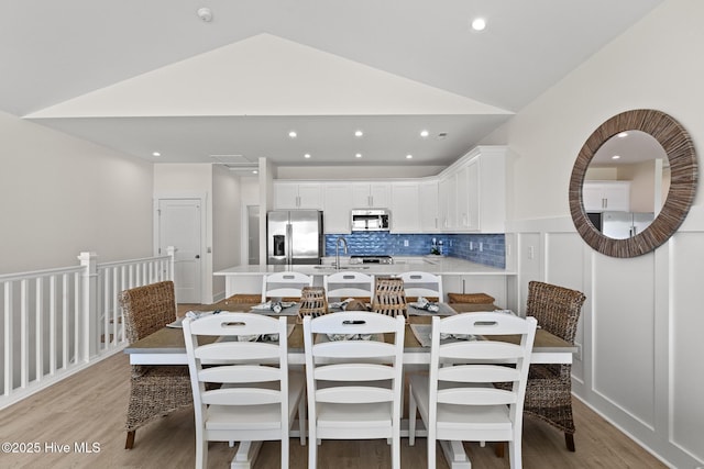 dining room featuring light wood-style floors, recessed lighting, vaulted ceiling, and a decorative wall