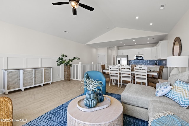 living area featuring lofted ceiling, a decorative wall, a wainscoted wall, visible vents, and light wood-style floors