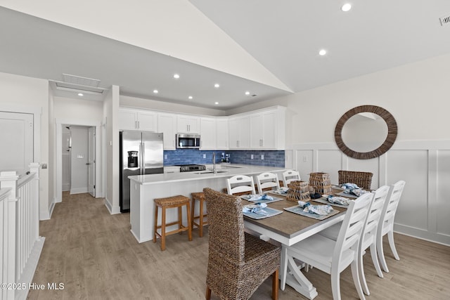 dining room featuring a wainscoted wall, visible vents, a decorative wall, light wood-style floors, and vaulted ceiling