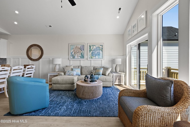 living room with lofted ceiling, a decorative wall, a wainscoted wall, wood finished floors, and visible vents