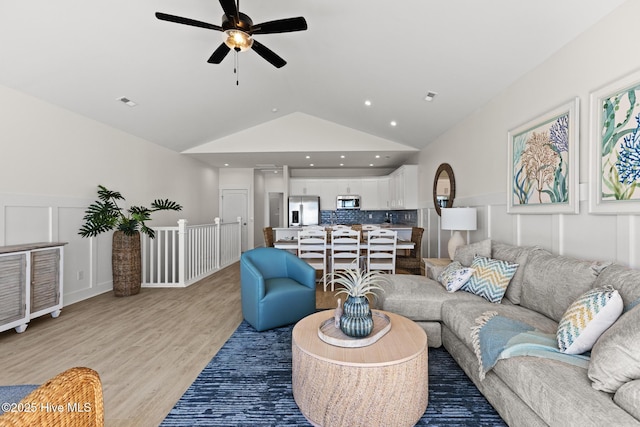 living area featuring recessed lighting, a decorative wall, light wood-style flooring, wainscoting, and vaulted ceiling