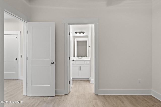 hall with light wood-style flooring, baseboards, and a sink