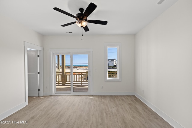 empty room with ceiling fan, light wood finished floors, visible vents, and baseboards