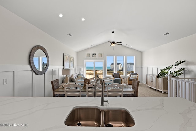 kitchen with a sink, visible vents, open floor plan, wainscoting, and light stone countertops