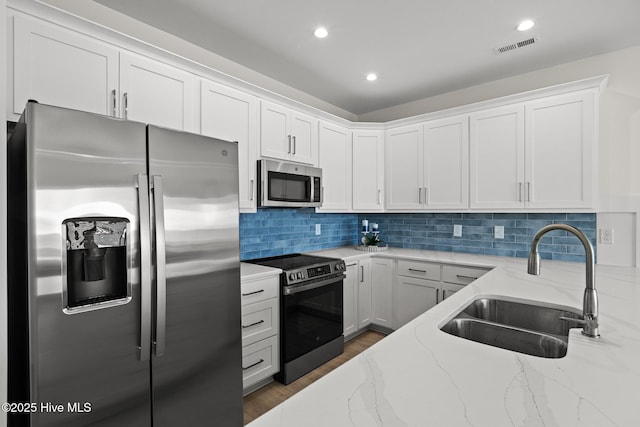 kitchen featuring light stone countertops, white cabinetry, appliances with stainless steel finishes, and a sink