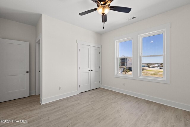 unfurnished bedroom with a closet, visible vents, light wood-style flooring, a ceiling fan, and baseboards